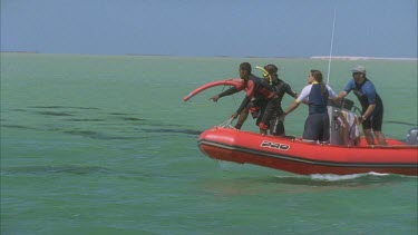 marine scientists on red zodiac inflatable boat heading out across bay pointing at dugong in water
