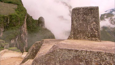 Part of the Machu Picchu ruins with terraced walls and cloud covered mountains in the background