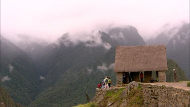 Tourists standing in and round a stone building over looking the mountains and valley surrounding Machu Picchu