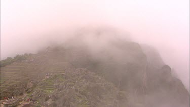 Time lapse of tourists walking on and around the stone terraces at a misty Machu Picchu