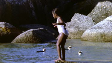 Girl jumps into water. Penguins swimming in bg.