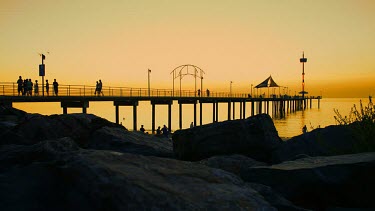 The busy activity of a popular jetty is contrasted by the serene movement of the shot behind a rocky silhouette. Pier.