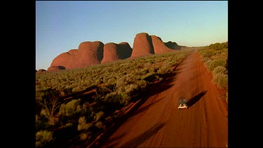 Four wheel drive drives down dirt road with Kata Juta in background.