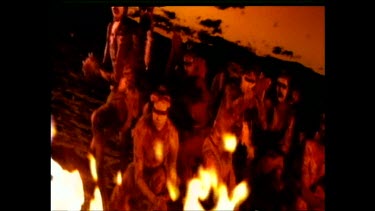 Aboriginal dance around a fire, sunset. Dancers bodies are painted white.