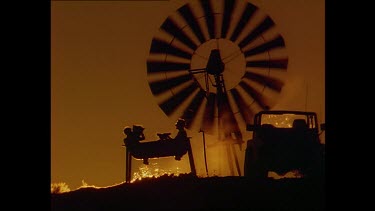 Sunset, Two people in a water trough below a large windmill.