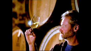 Vintner checks wine fermenting in barrels. Has a drink of wine. Wine cask inspection.