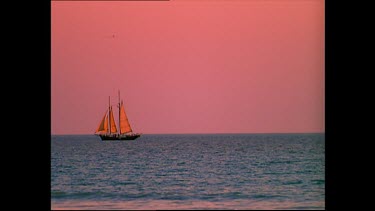 Sail boat on calm seas with pink sky in background