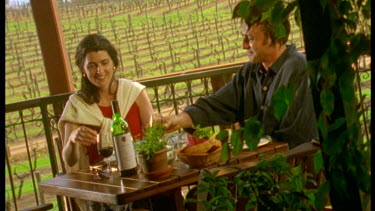 Couple eating lunch on verandah with vineyards in background. Margaret River