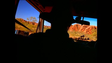 POV from interior of car. Man with hat in silhouette, driving through Bungle Bungle mountain range. Purnululu National Park