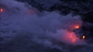 Where the edge of the Kilauea lava delta meets the ocean a line of steam rises into the air.