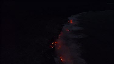 Where the edge of the Kilauea lava delta meets the ocean a line of steam rises into the air. Night.