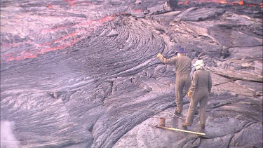 Scientists  throwing equipment into lava flow. They pull out some lava and quickly cool it.