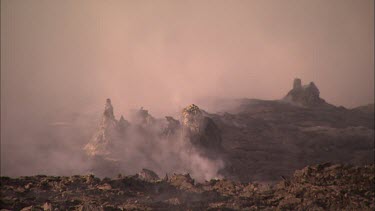 Apocalyptic landscape. Steam and smoke rising from a vent in the lava crust. Dark volcanic rocky landscape. Eerie. the sky is pink, tinted by the sun and the smoke.
