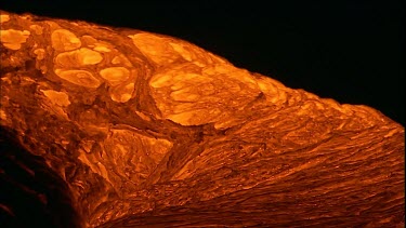 The molten rock incandescent lava moving across the surface. It looks plastic in form, soft and maleable as if it is being extruded. Bubbling out of the earth.