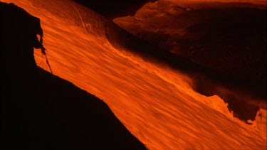 A river of incandescent lava flowing down a lava channel. Night