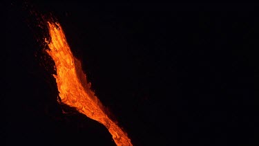 A river of incandescent lava flowing down a lava channel. Night